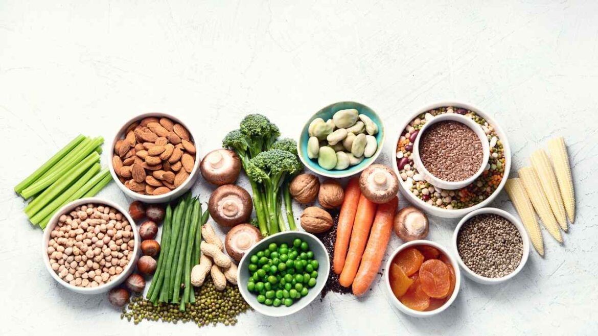 Fresh vegetables, legumes, nuts and plant-based protein sources arranged on white marble surface