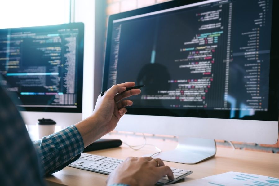 A programmer pointing at lines of code on a monitor while developing AI design software.