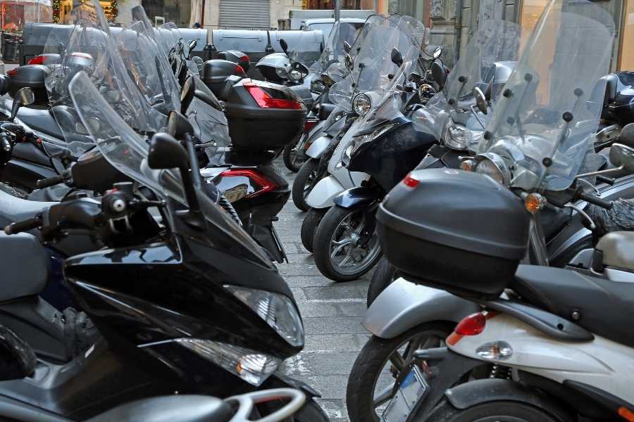 A dense row of parked scooters lined up on a city street, most featuring tall protective motorcycle screens.